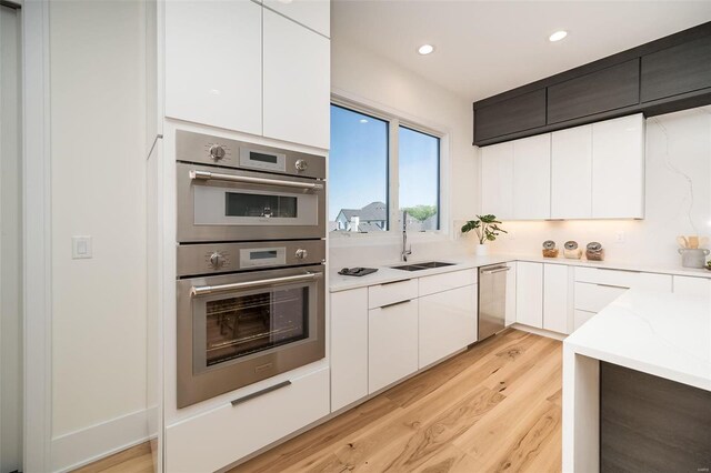 kitchen with appliances with stainless steel finishes, a sink, light wood-style flooring, modern cabinets, and white cabinets