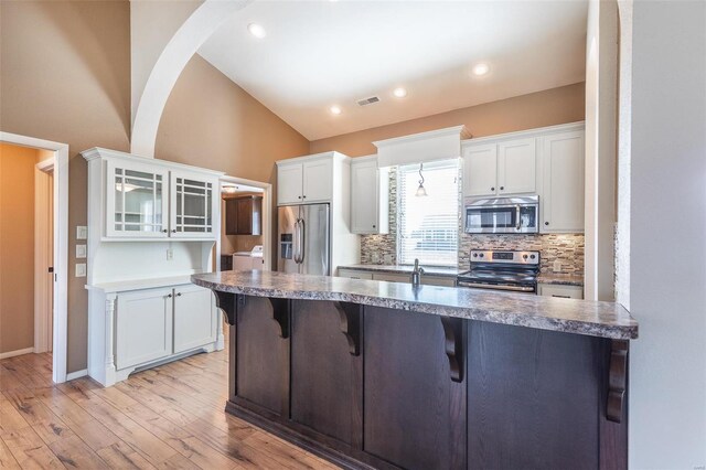 kitchen with appliances with stainless steel finishes, lofted ceiling, a breakfast bar area, white cabinetry, and light wood finished floors