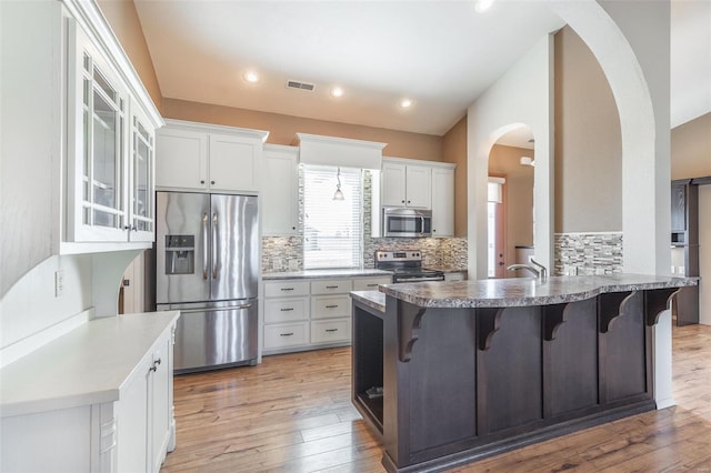 kitchen featuring stainless steel appliances, arched walkways, a peninsula, a kitchen bar, and recessed lighting