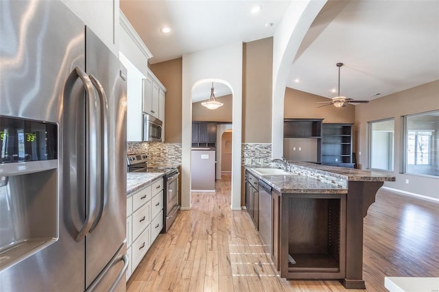 kitchen featuring stainless steel appliances, arched walkways, a sink, decorative backsplash, and lofted ceiling