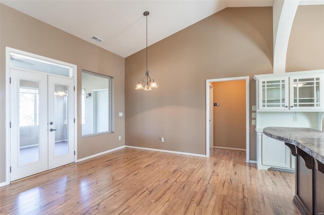 unfurnished dining area with light wood finished floors, french doors, a chandelier, high vaulted ceiling, and baseboards