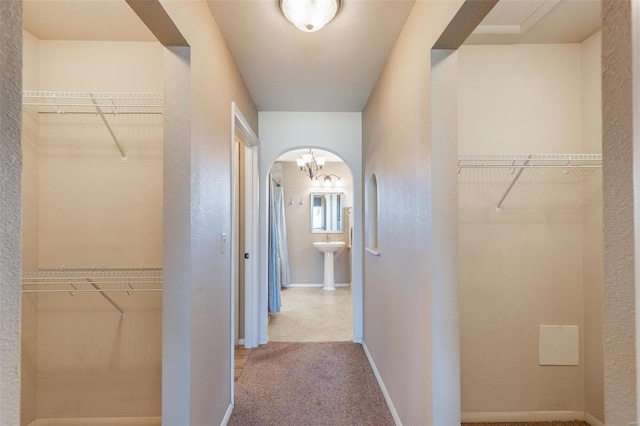 hall with a textured wall, arched walkways, baseboards, carpet, and a sink
