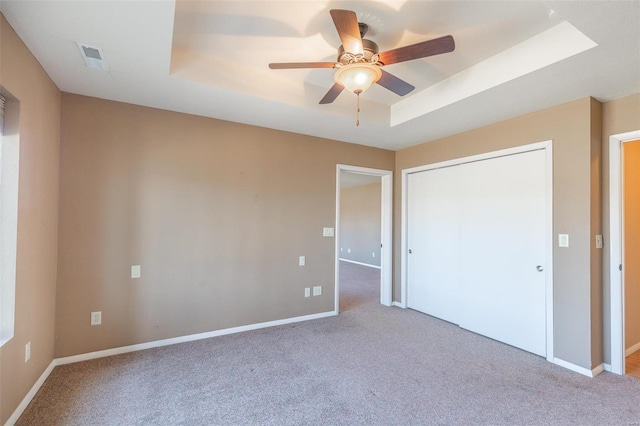 unfurnished bedroom with a tray ceiling, carpet flooring, baseboards, and a ceiling fan