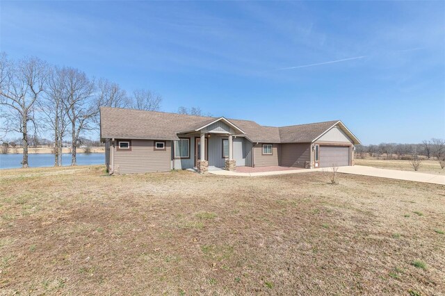 ranch-style home featuring a garage, a front yard, concrete driveway, and a water view