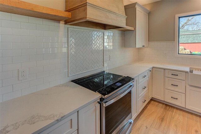115 S Taylor St, Red Bud, IL 62278 - kitchen featuring stainless steel electric range oven, light wood finished floors, tasteful backsplash, custom exhaust hood, and light stone counters