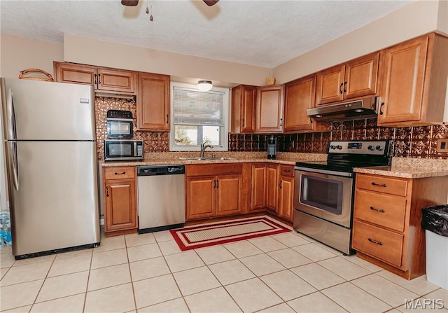 12561 Carroll Dr, Rolla, MO 65401 - kitchen featuring appliances with stainless steel finishes, under cabinet range hood, a sink, brown cabinetry, and a textured ceiling