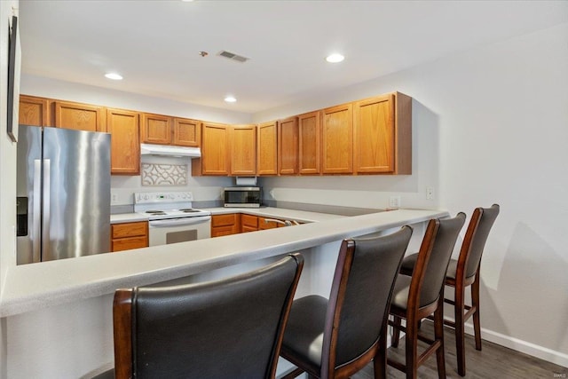 kitchen featuring stainless steel appliances, a peninsula, dark wood-style flooring, baseboards, and under cabinet range hood