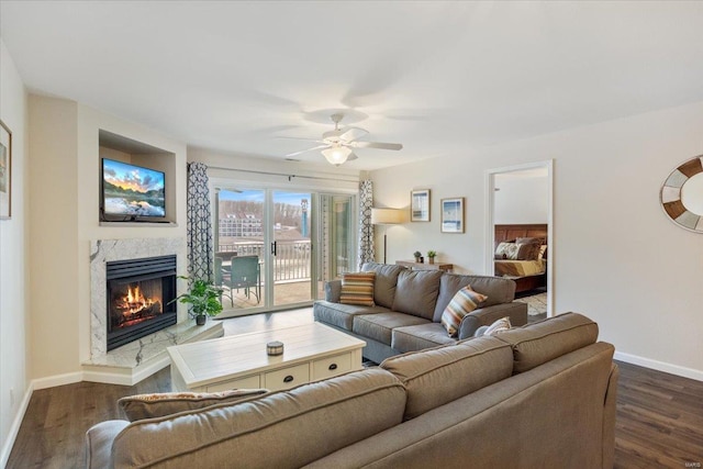 living area with a premium fireplace, a ceiling fan, baseboards, and dark wood-style floors