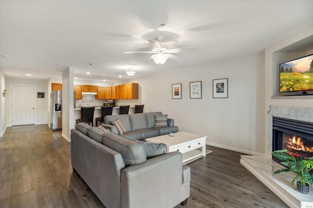 living room with dark wood-type flooring, baseboards, a ceiling fan, a fireplace, and recessed lighting