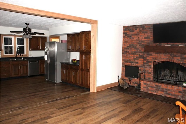 462 Il Route 127, Greenville, IL 62246 - kitchen featuring appliances with stainless steel finishes, dark countertops, a brick fireplace, a textured ceiling, and dark wood-type flooring