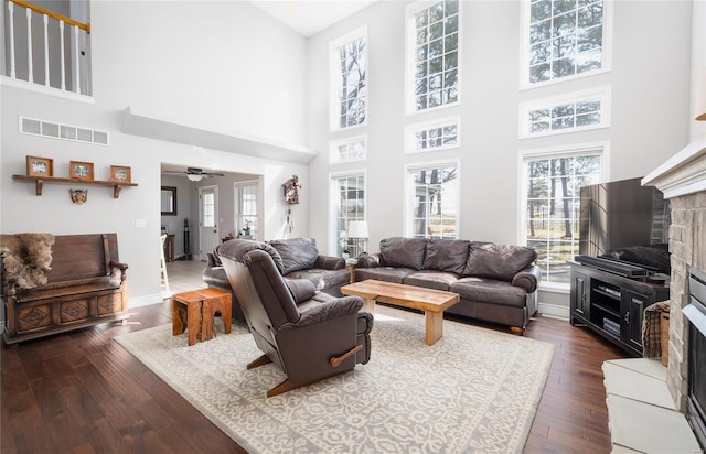 living area featuring a fireplace with raised hearth, ceiling fan, dark wood finished floors, a high ceiling, and baseboards