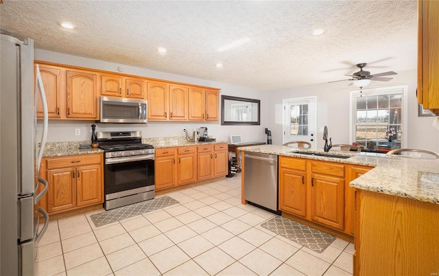 kitchen with appliances with stainless steel finishes, a sink, a ceiling fan, light stone counters, and a textured ceiling