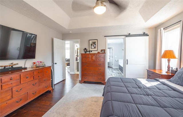bedroom featuring dark wood-style floors, a barn door, a tray ceiling, a textured ceiling, and baseboards