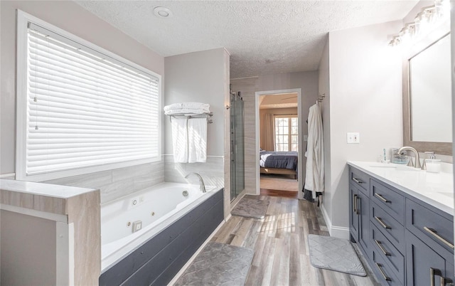 ensuite bathroom with a jetted tub, a textured ceiling, double vanity, a shower stall, and wood finished floors