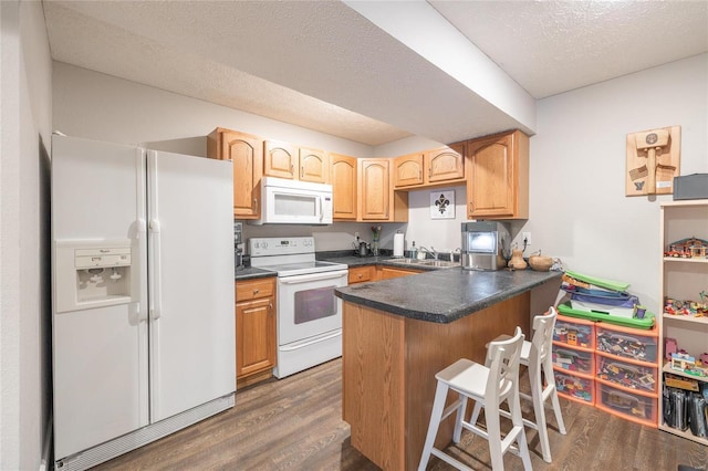 kitchen featuring white appliances, dark countertops, dark wood-style floors, a sink, and a kitchen breakfast bar