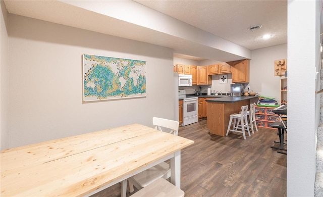 kitchen featuring white appliances, dark wood-style flooring, a breakfast bar area, dark countertops, and a peninsula