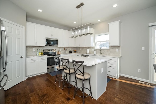 kitchen with stainless steel appliances, a sink, a center island, a kitchen bar, and white cabinets