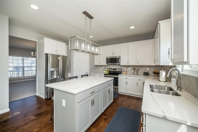 kitchen with stainless steel appliances, a sink, a kitchen island, light stone counters, and recessed lighting