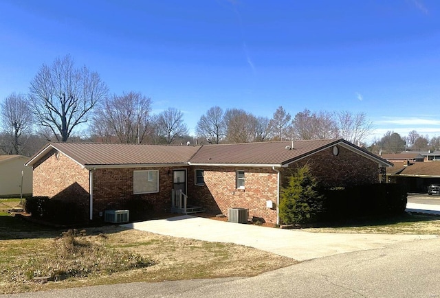 ranch-style house featuring brick siding, cooling unit, metal roof, and driveway