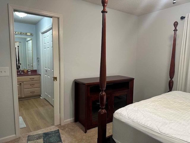 bedroom with light carpet, ensuite bathroom, a textured ceiling, and baseboards