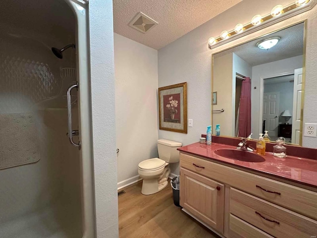 bathroom featuring a shower stall, wood finished floors, vanity, toilet, and a textured ceiling