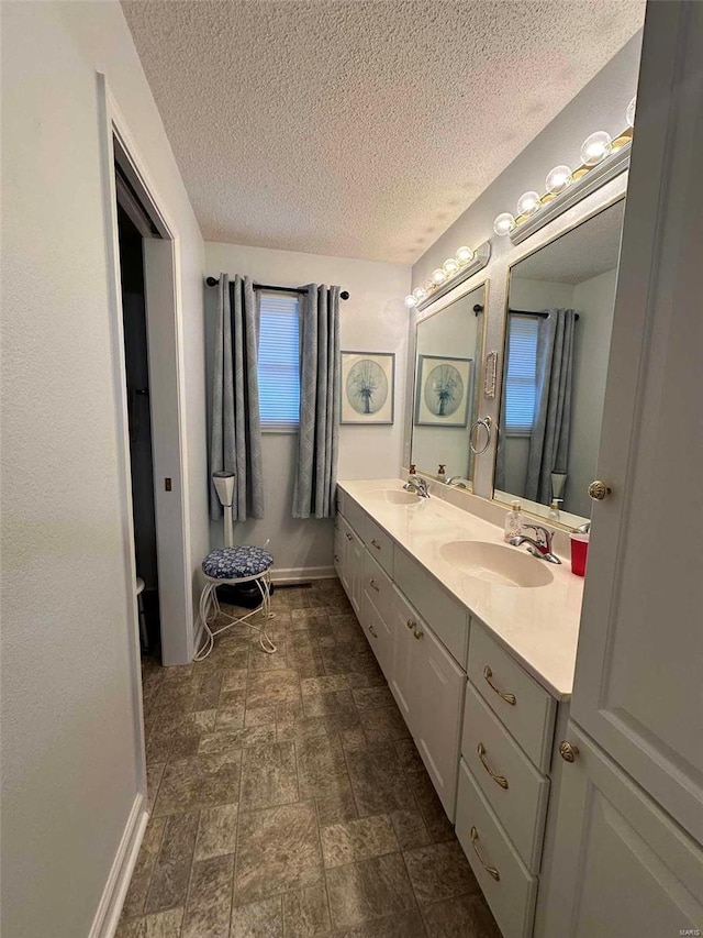 full bathroom featuring a textured ceiling, baseboards, double vanity, and stone finish floors