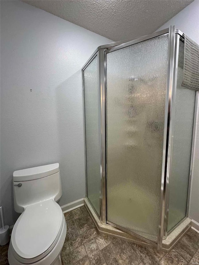 bathroom featuring a textured ceiling, a shower stall, toilet, and baseboards