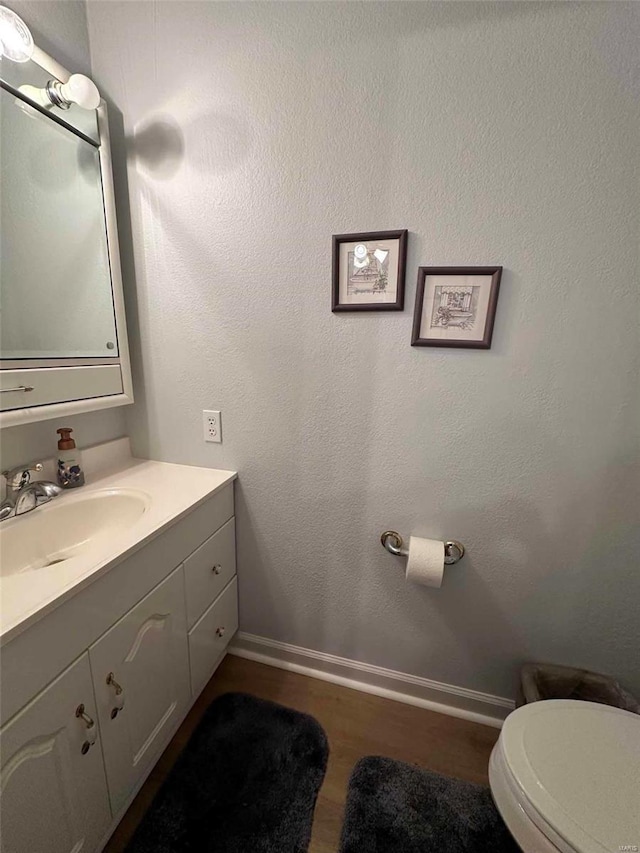 bathroom with wood finished floors, baseboards, vanity, and toilet