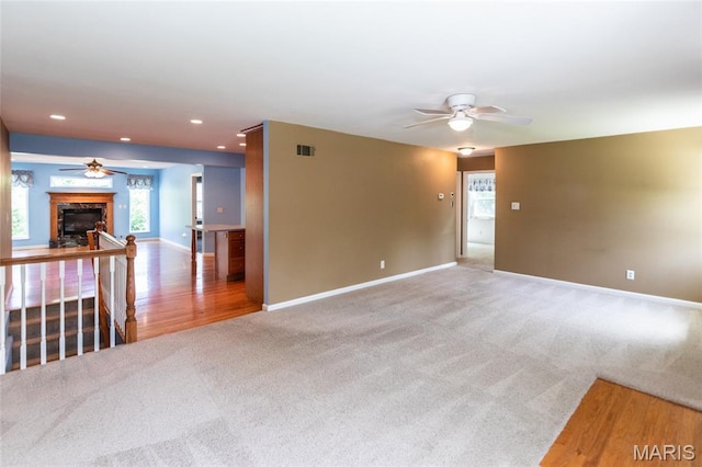 carpeted spare room featuring a ceiling fan, baseboards, a fireplace, wood finished floors, and recessed lighting