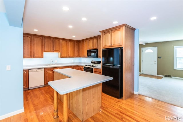 kitchen featuring black appliances, a sink, light countertops, a kitchen island, and recessed lighting