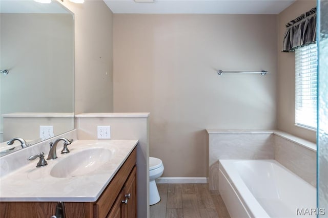 full bathroom with toilet, a bath, wood finished floors, vanity, and baseboards