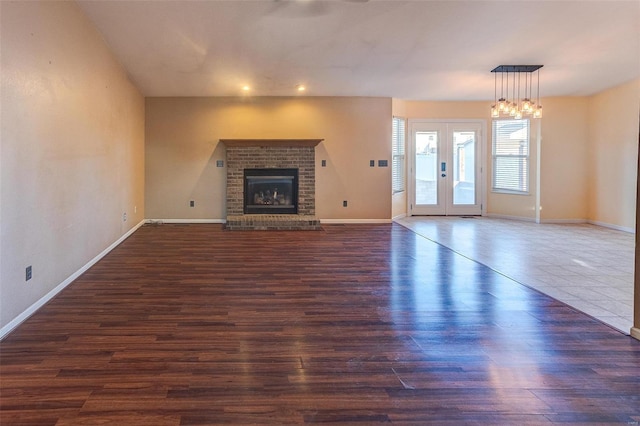 unfurnished living room with dark wood finished floors, a brick fireplace, french doors, baseboards, and recessed lighting