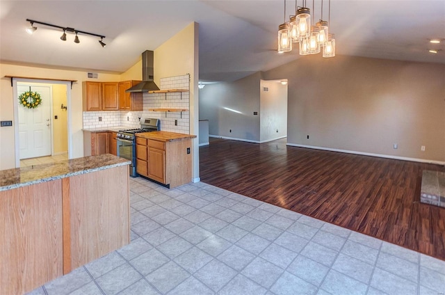 kitchen with stainless steel gas range oven, wall chimney range hood, track lighting, lofted ceiling, and brown cabinetry