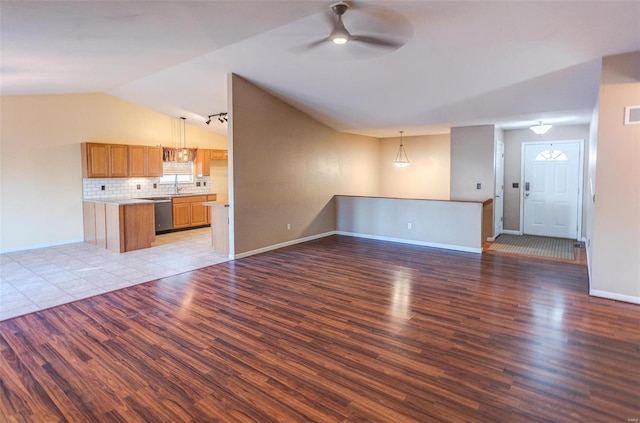 unfurnished living room with a ceiling fan, vaulted ceiling, wood finished floors, a sink, and baseboards