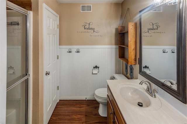 full bath featuring wood finished floors, a wainscoted wall, vanity, a shower stall, and toilet