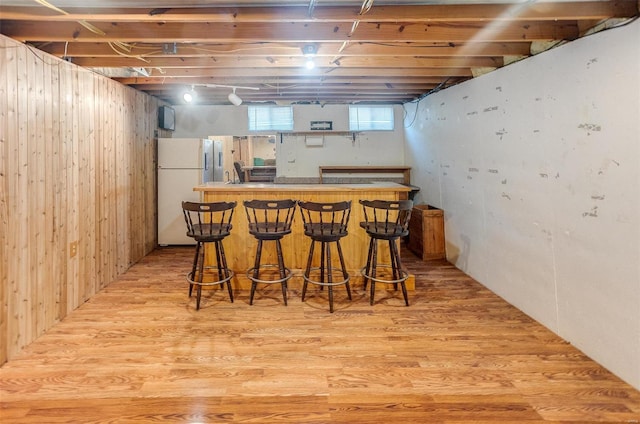 indoor dry bar featuring freestanding refrigerator, light wood-style floors, and wood walls