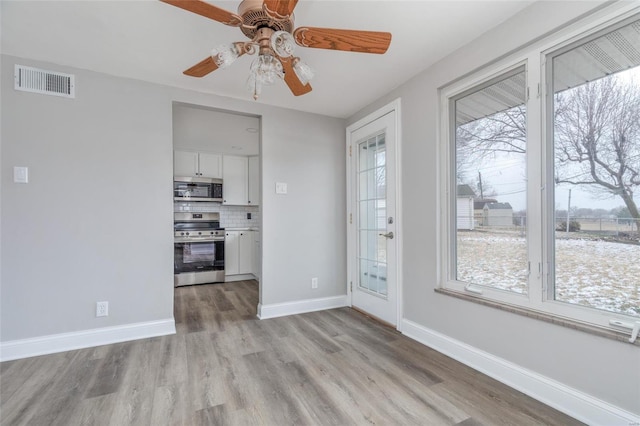 unfurnished dining area featuring healthy amount of natural light, light wood-style flooring, a ceiling fan, and baseboards