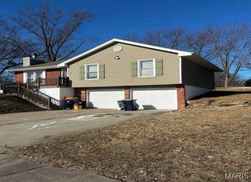 208 NE 80th St, Kansas City, MO 64118 - view of side of home with an attached garage, concrete driveway, brick siding, stairs, and a chimney