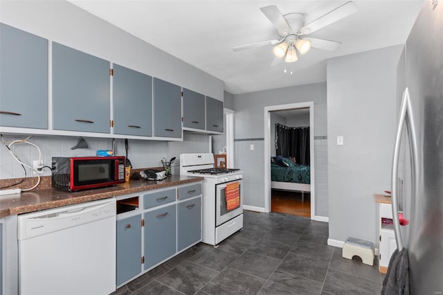 kitchen with white appliances, blue cabinets, dark countertops, and a ceiling fan