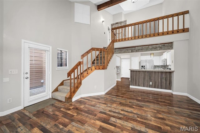 unfurnished living room featuring a towering ceiling, stairway, dark wood finished floors, baseboards, and beamed ceiling