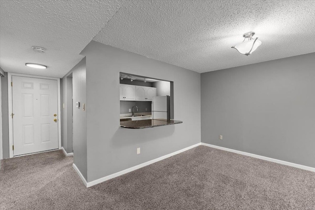 carpeted empty room with a textured ceiling, a sink, baseboards, and a smoke detector