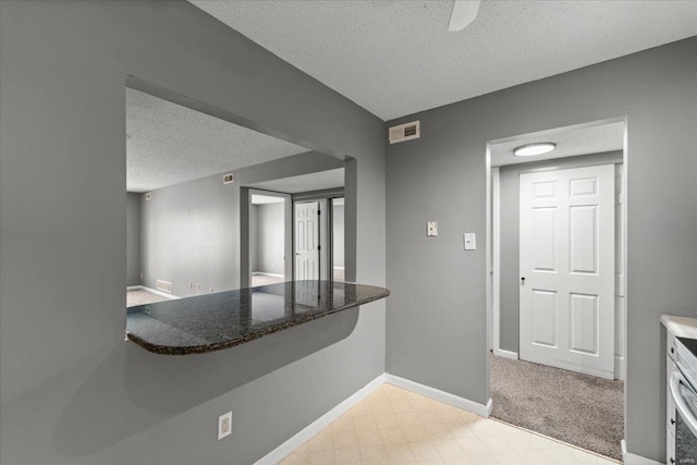hall featuring a textured ceiling, baseboards, and light floors