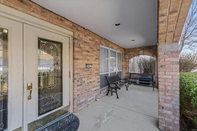 view of exterior entry with brick siding and covered porch