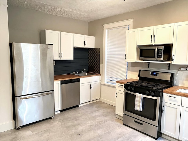 5727 Dewey Ave, Saint Louis, MO 63116 - kitchen featuring appliances with stainless steel finishes, wood counters, a sink, white cabinets, and a textured ceiling