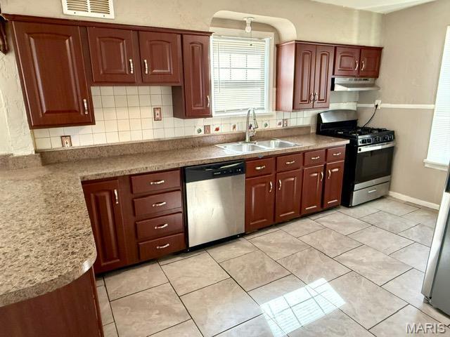 19 S Schlueter Ave, Saint Louis, MO 63135 - kitchen with stainless steel appliances, under cabinet range hood, decorative backsplash, light tile patterned floors, and arched walkways