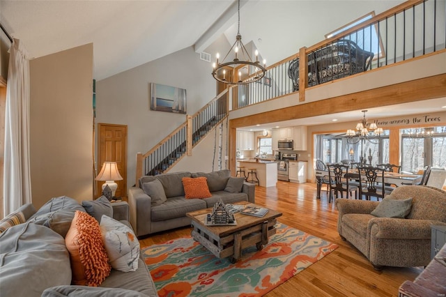 living room with a chandelier, high vaulted ceiling, light wood finished floors, stairs, and beamed ceiling