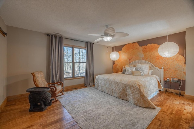 bedroom with wood finished floors, baseboards, a ceiling fan, and a textured ceiling