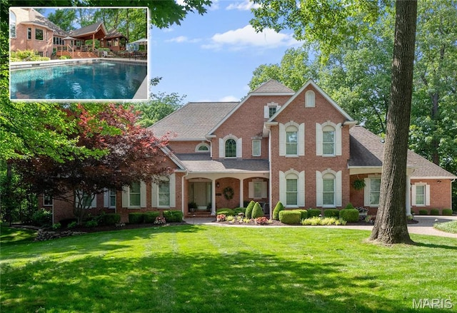 view of front of property featuring brick siding, a front yard, roof with shingles, and an outdoor pool