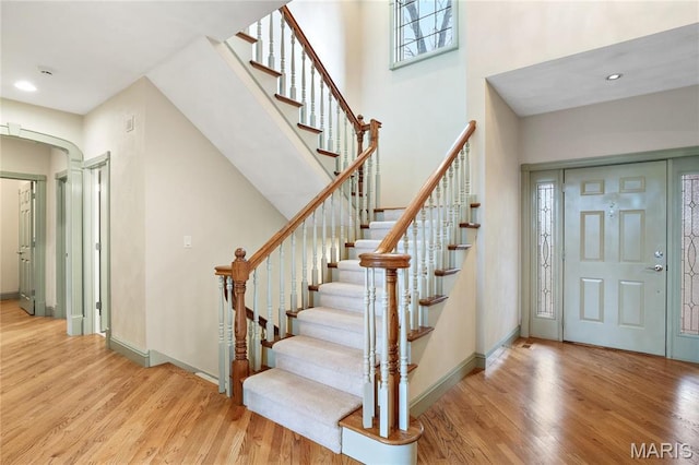 foyer featuring wood finished floors, stairway, arched walkways, recessed lighting, and a towering ceiling