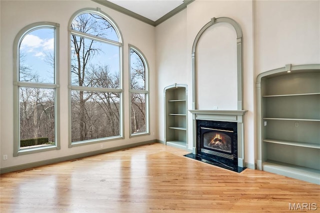 unfurnished living room featuring wood finished floors, ornamental molding, a fireplace, built in shelves, and baseboards